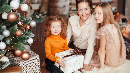 mother and her daughters opening a gift box near the Christmas tの写真素材