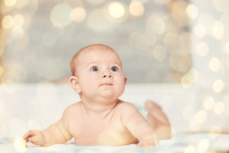pretty baby lying surprised looking at the new world. beautiful bokeh effect from a garlandの写真素材