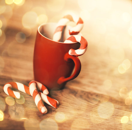 Christmas mug and candle on wooden background. beautiful bokeh effect from a garland.の写真素材