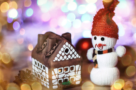toy snowman and gingerbread house at the Christmas table. beautiful bokeh effect from a garland.の写真素材