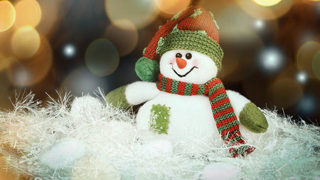 cute toy snowman on a black background. beautiful bokeh effect from a garland.の写真素材