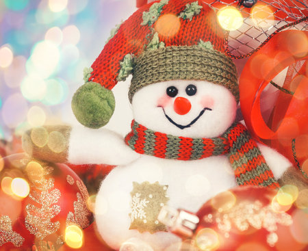 funny snowman on the background of red Christmas balls. beautiful bokeh effect from a garland.の写真素材