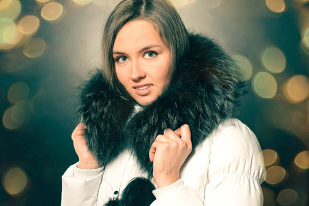 portrait of beautiful young woman in winter jacket. Beautiful bokeh effect from a garland.の写真素材