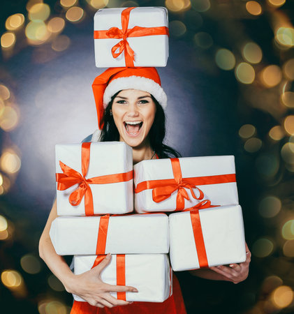 happy young woman in costume of Santa Claus with lots of Christmas. Beautiful bokeh effect from a garland.の写真素材