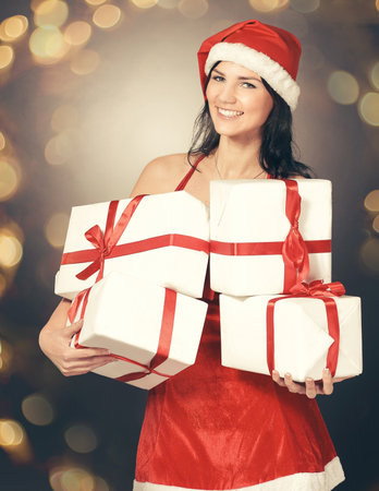 happy young woman in costume of Santa Claus with lots of Christmas shopping. Beautiful bokeh effect from a garland.の写真素材