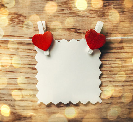 blank note on clothespin on wooden background. beautiful bokeh effect from a garland.の写真素材