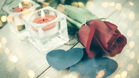 red rose and two blue hearts on a light wooden background. Beautiful bokeh effect from a garland.の写真素材
