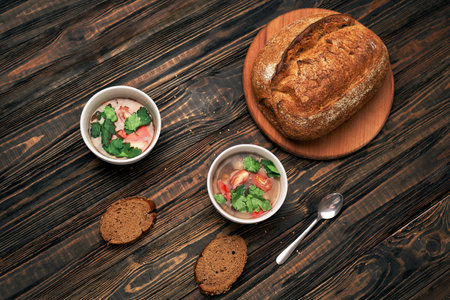 two plates of tomato soup and bread on a wooden board.の写真素材