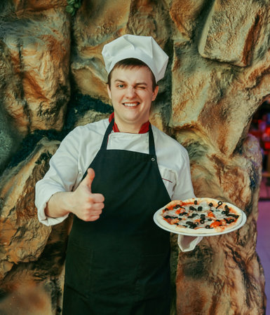 chef holds a large pizza and shows a thumb upの写真素材