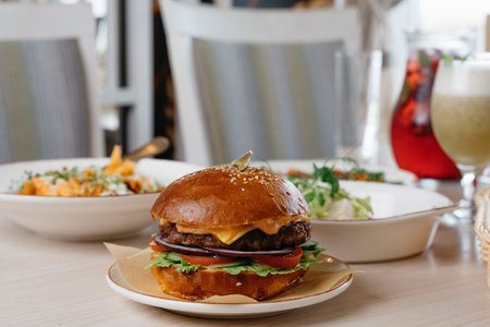 Tasty juicy burger with cocktails on the table with other dishes.lunch.front view. light chairs in the backgroundの写真素材