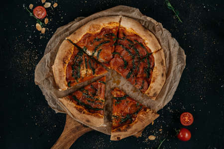 Delicious pepperoni pizza and basil tomato with cooking ingredients on a black background. Top view of hot pepperoni pizza.の写真素材