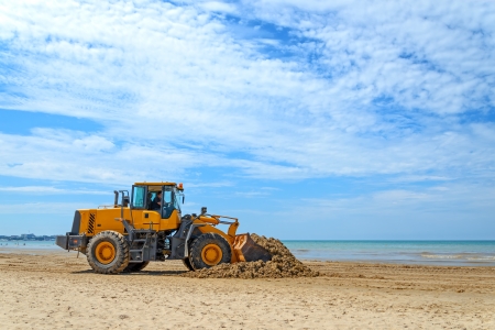 The bulldozer cleans dirt on a beach after a stormの写真素材