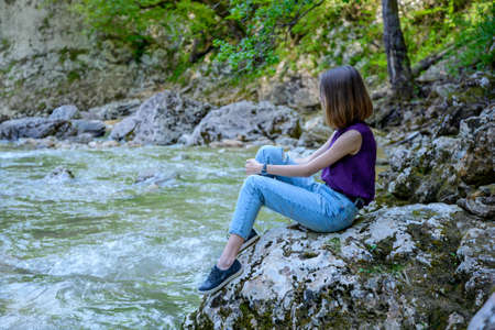 A girl sits on a stone near a mountain riverの写真素材