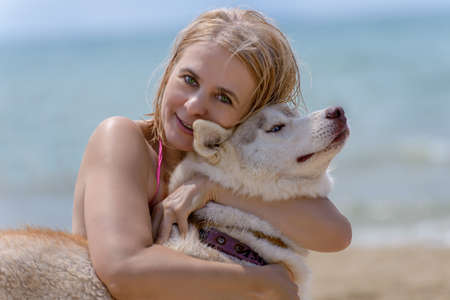 Woman in pink bikini hugging a dog Husky on the beachの写真素材