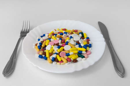 A bunch of pills lying on a plate, next to a fork and a knifeの写真素材