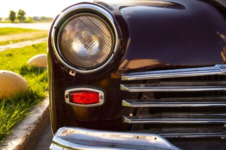Headlight, chrome grille. An old car is parked at the curb. Retro and lush green grassの写真素材