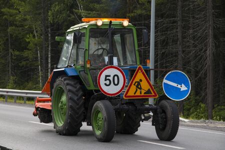 A wheeled tractor with warning signs installed on it stands at the site of road repair.の写真素材