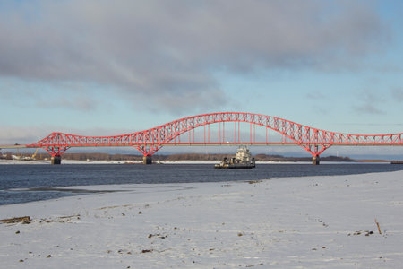 A tugboat against the background of the bridge in Ugra. A tugboat on a river with snowy shores...