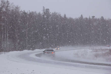 A road covered by a blizzard. Cars drive along the highway in the North in heavy snow.の写真素材
