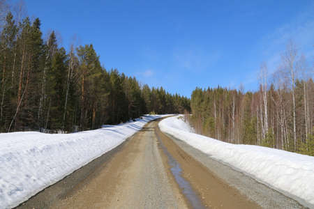 Spring road in the Urals in the forest. A dirt road passes through picturesque landscapes in the Ural forest among melting snows.の写真素材