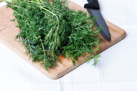 Dill on a cutting board ceramic knife on a white tablecloth.の写真素材