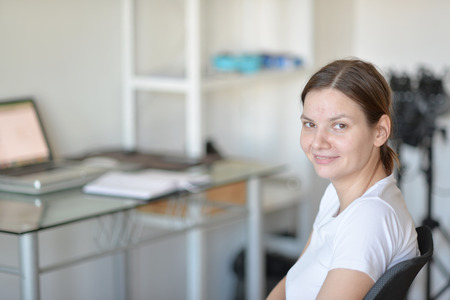The girl in a white shirt sits at a table with a computer.の写真素材