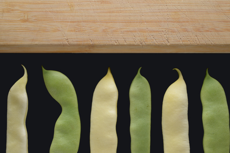 Yellow and green beans on a cutting board. Black background.