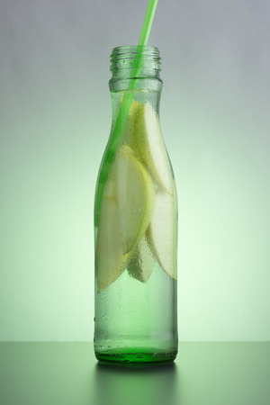 Green bottle with natural apple lemonade on the table. Slices of green apple in a bottle with a straw.の写真素材