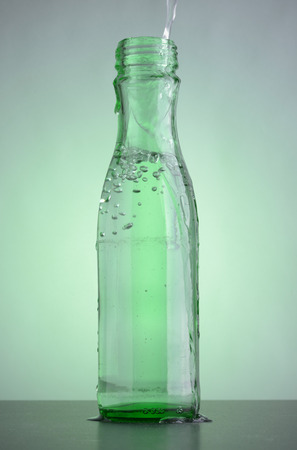 Green bottle with clean drinking water on the table. Bubbles in the glass transparent bottle.の写真素材
