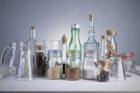 Still life of transparent glass bottles, cans and glasses on a white wooden table.の写真素材