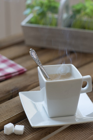 Hot morning coffee in a square dish on a wooden table with a napkin klechatoy and green plants.の写真素材
