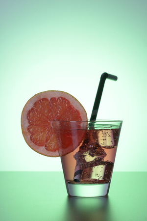 Fresh cocktail with grapefruit, ice and striped drinking straw on a green background.の写真素材