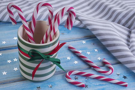 Striped ceramic cup with candy canes on a blue wooden table.の写真素材