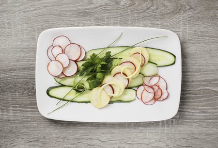 Summer salad of cucumbers, radishes, kohlrabi with parsley on a white oblong plate.の写真素材