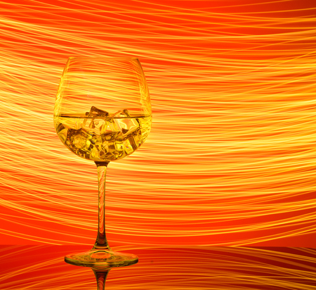 A glass with a drink and ice cubes on a red background with golden lights.の写真素材