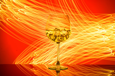 A glass with a drink and ice cubes on a red background with golden lights.の写真素材