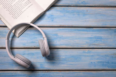 White headphones and a white book on the blue and beige background. Audio book reading online.の写真素材