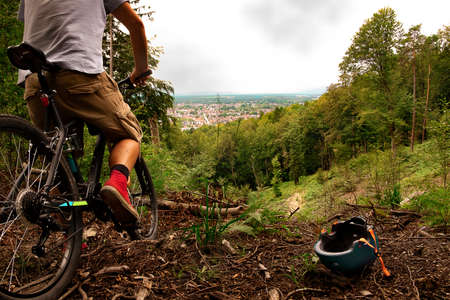 A cyclist with his helmet removed looks at the road in front of him. The helmet is on the ground.の写真素材