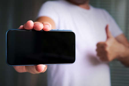 A man in a pink plaid shirt with a cell phone in his hand. White T-shirt.の写真素材