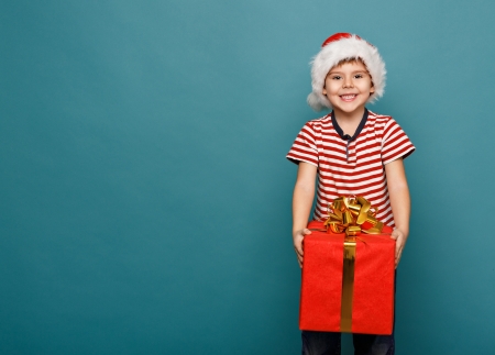 Smiling  funny child in Santa red hat holding Christmas gift in hand. Christmas concept.の写真素材