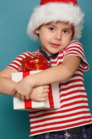 Smiling  funny child in Santa red hat holding Christmas gift in hand. Christmas concept.の写真素材
