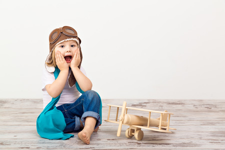 Beautiful smiling child (girl) in helmet on a white background playing with a plane. Vintage pilot (aviator) conceptの写真素材