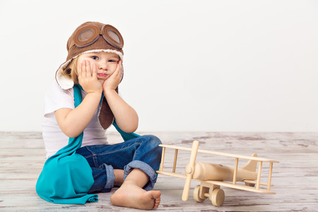 Beautiful smiling child (girl) in helmet on a white background playing with a plane. Vintage pilot (aviator) conceptの写真素材