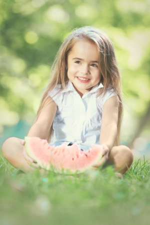 Happy smiling child playing in park on green grass and eating fruitsの写真素材