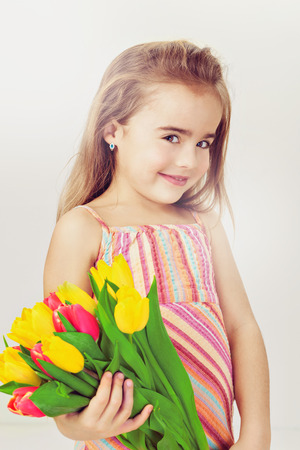Fashion baby face beautiful child with fair hair in a pink dress holds flowersの写真素材