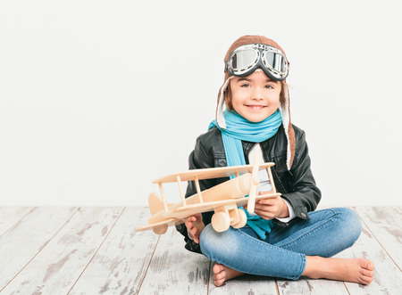 Beautiful smiling child (kid, girl) in helmet on a white background playing with a plane. Vintage pilot (aviator) conceptの写真素材