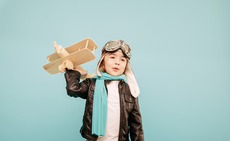 Beautiful smiling child (kid, girl) in helmet on a blue background playing with a plane. Vintage pilot (aviator) conceptの写真素材