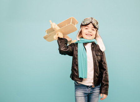 Beautiful smiling child (kid, girl) in helmet on a blue background playing with a plane. Vintage pilot (aviator) conceptの写真素材