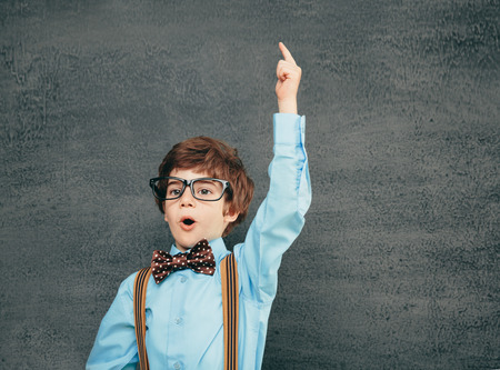 Cheerful smiling little kid (boy) against chalkboard. Looking at camera. School concept