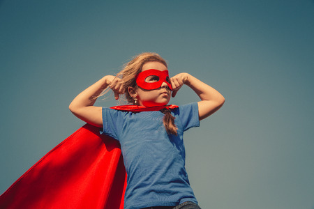 Funny little power super hero child (girl) in a red raincoat. Superhero concept.